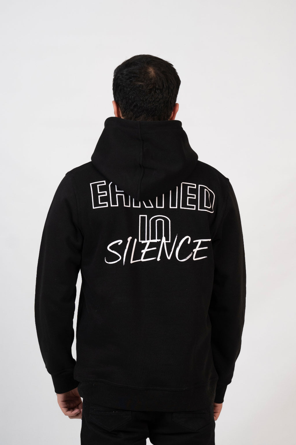 Person wearing a black hoodie with 'Humbled in Silence' text on the back against a white background