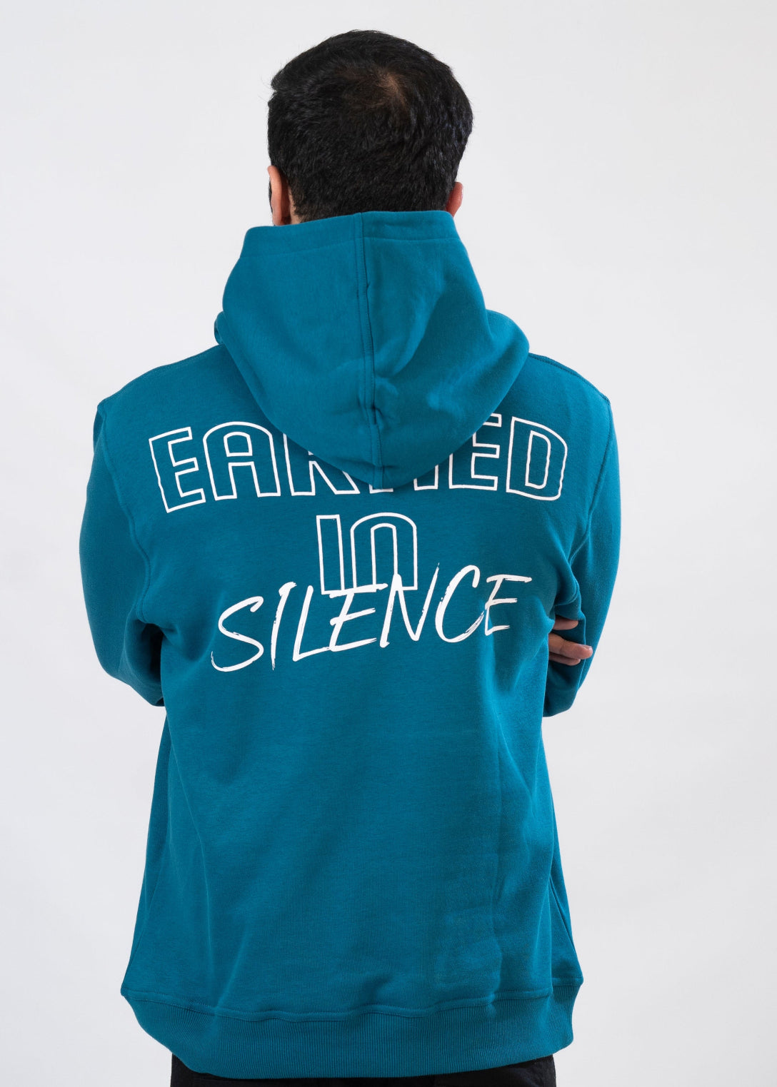 Person wearing a blue hoodie with 'EARNED IN SILENCE' text on the back against a white background