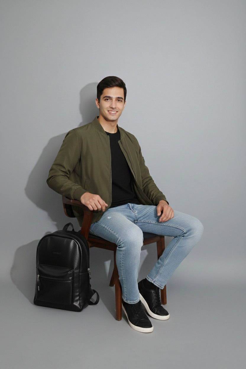 Man sitting on a chair with a black backpack next to him against a gray background