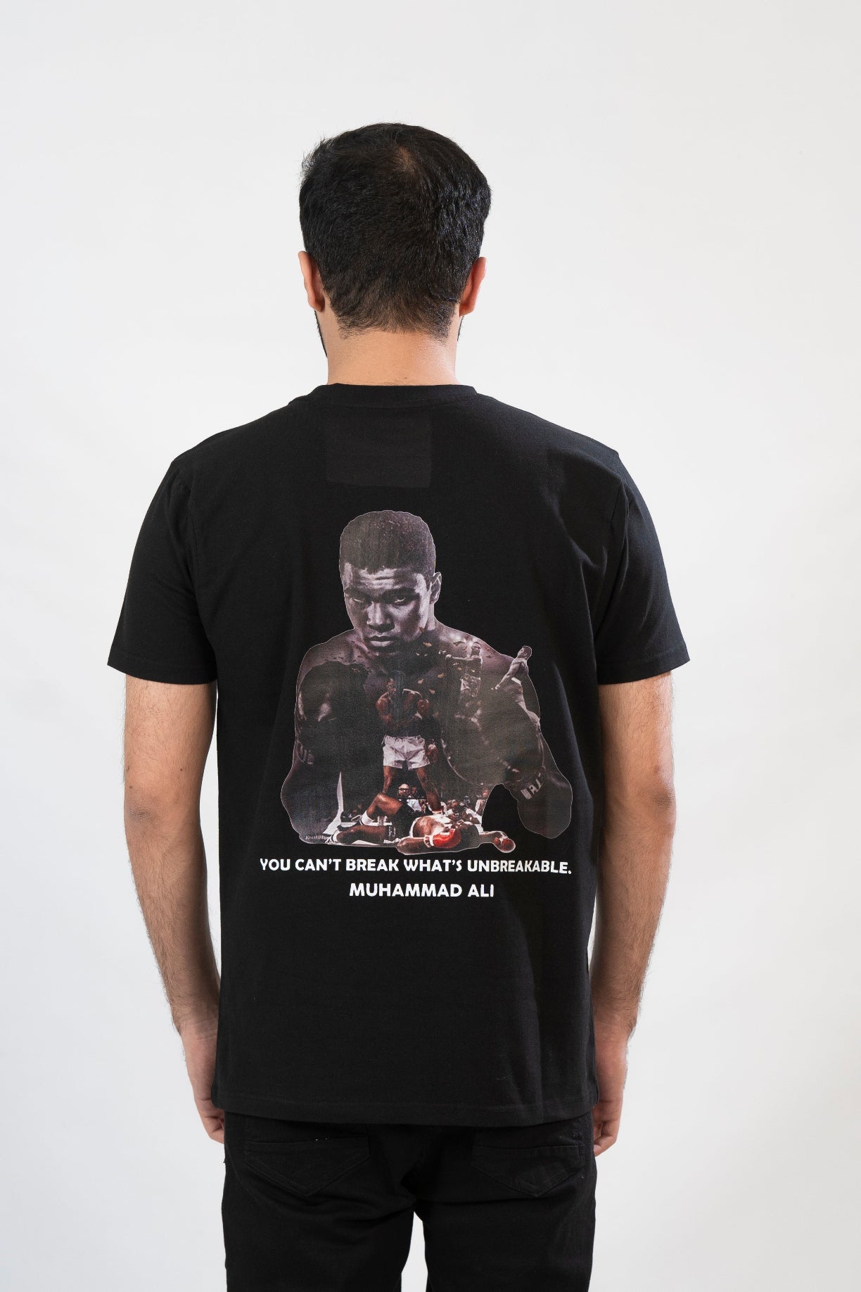 Person wearing a black t-shirt with a graphic design and text on the back, standing against a white background.
