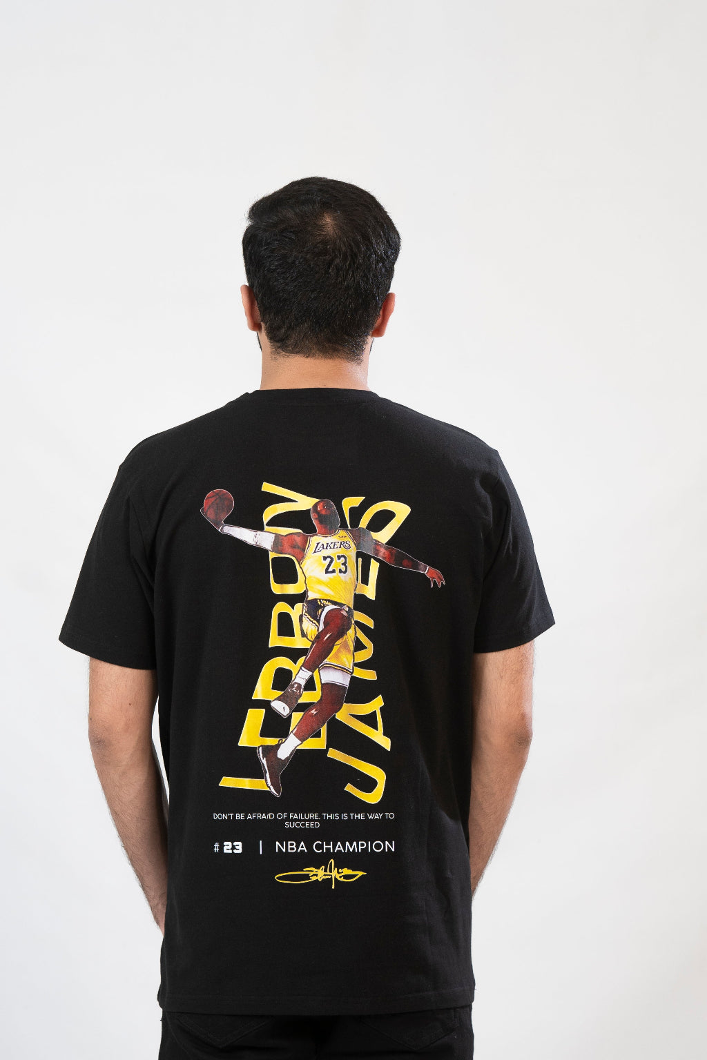 Person wearing a black t-shirt with a graphic of a basketball player and text on the back, on a white background.