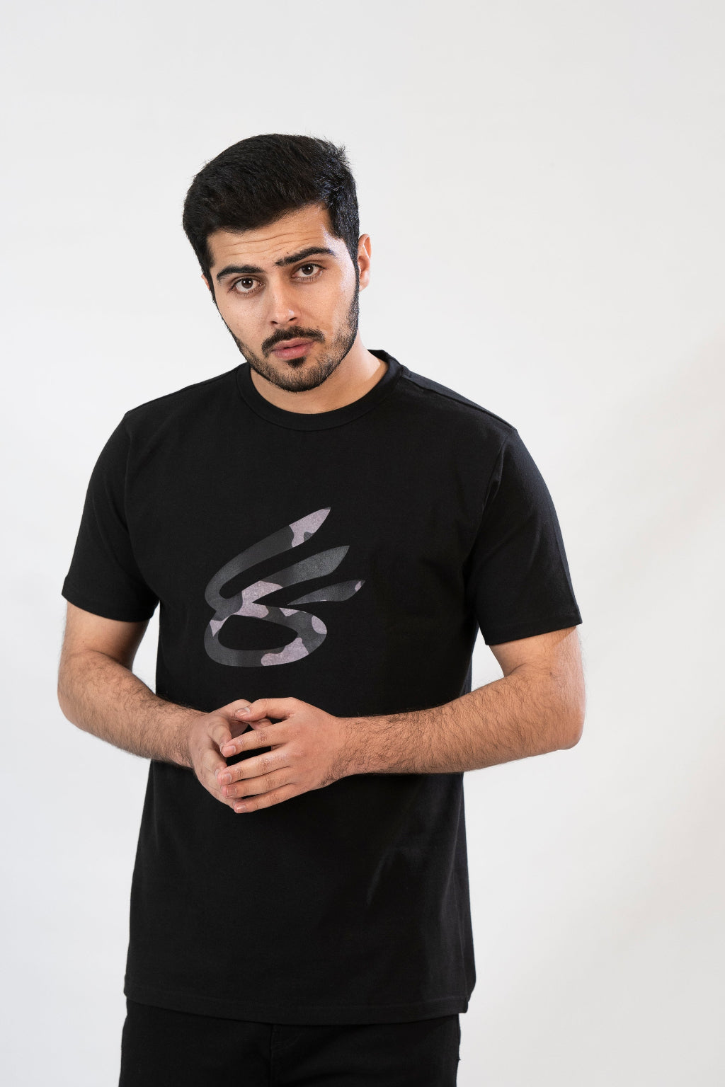 A man standing, wearing a black crew neck t-shirt with a geometric design on the front.