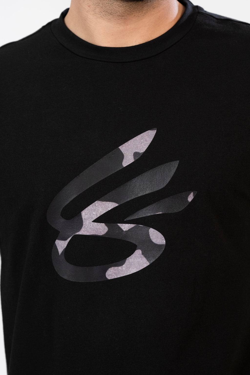 A man standing, wearing a black crew neck t-shirt with a geometric design on the front.
