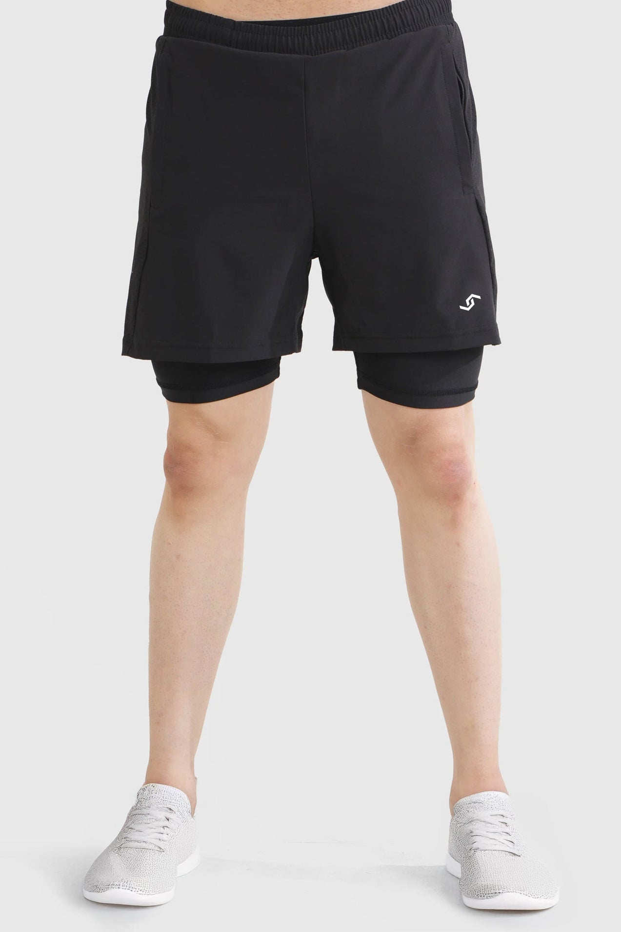 Person wearing black athletic shorts with a white logo on a light gray background