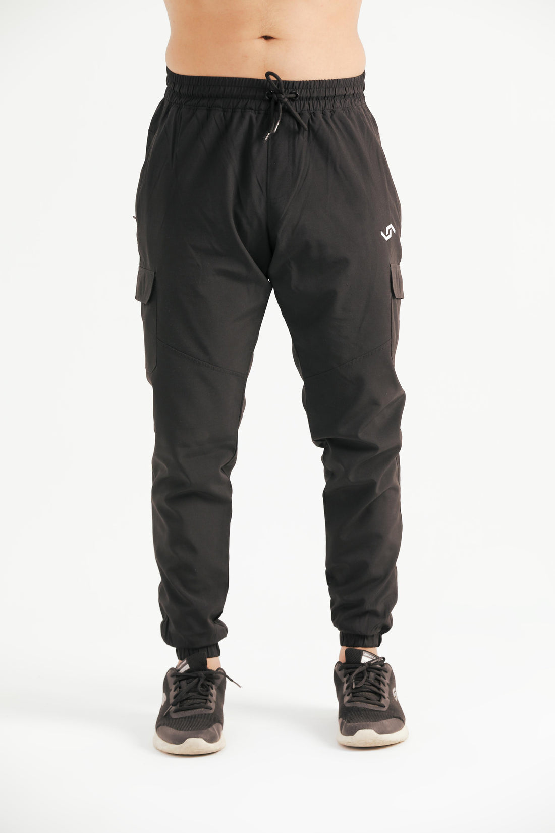A person standing against a white background wearing black leisure cargo pants with a drawstring waist and elastic bottom cuffs, paired with a white top and sneakers.