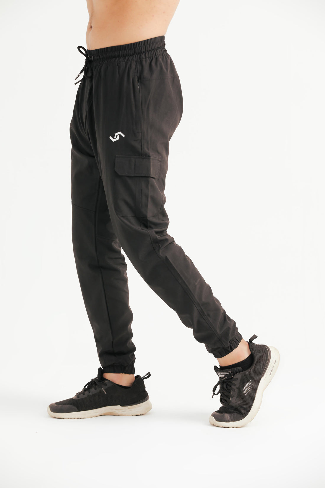 A person standing against a white background wearing black leisure cargo pants with a drawstring waist and elastic bottom cuffs, paired with a white top and sneakers.