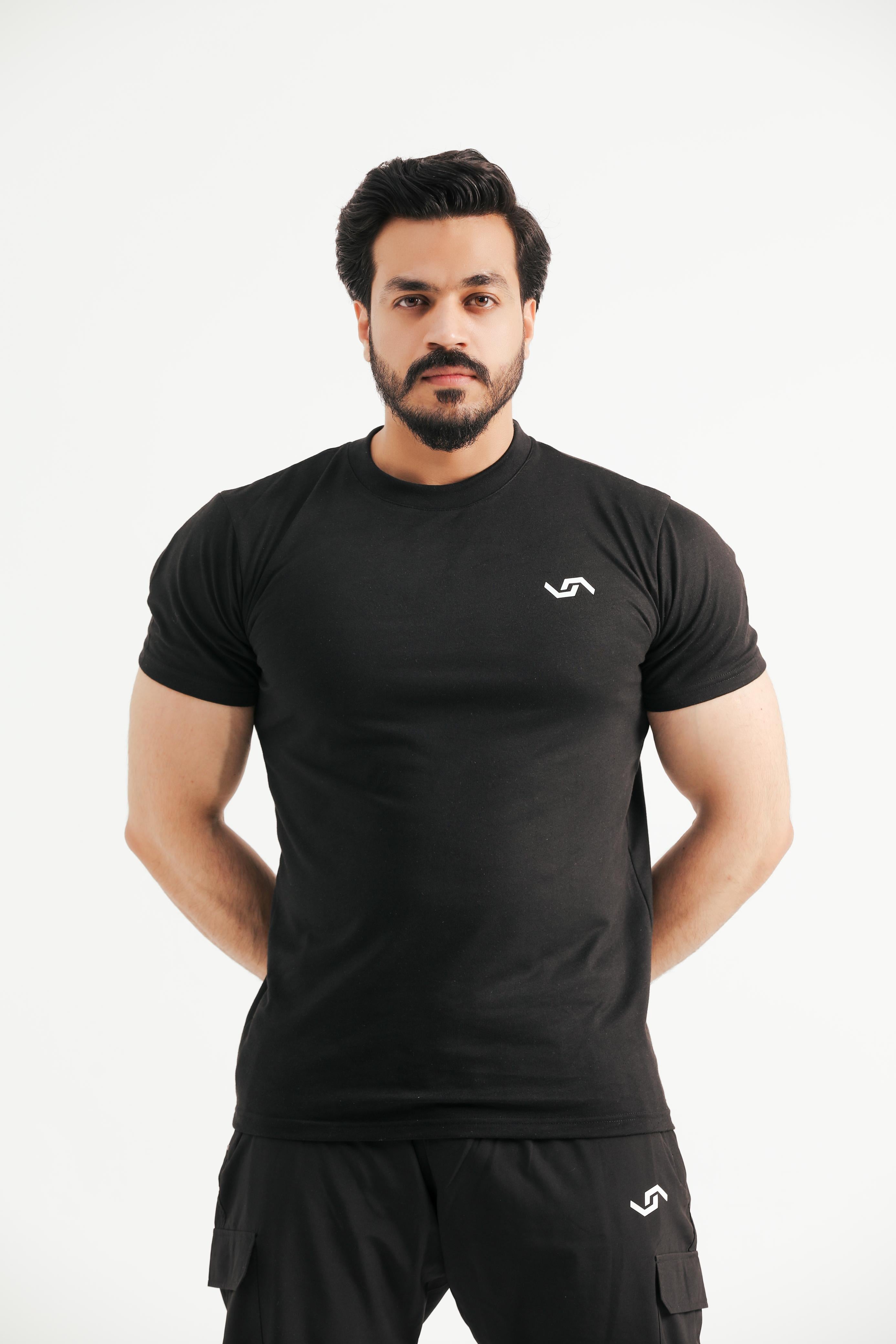A man wearing a black crew neck t-shirt with a logo on the chest and short black pants.