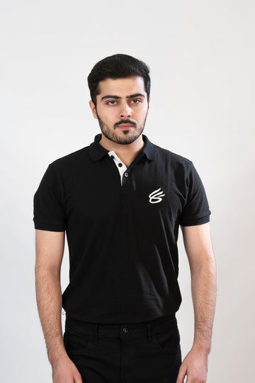 A person wearing a black polo shirt with a white collar and a logo on the chest, standing against a neutral background.