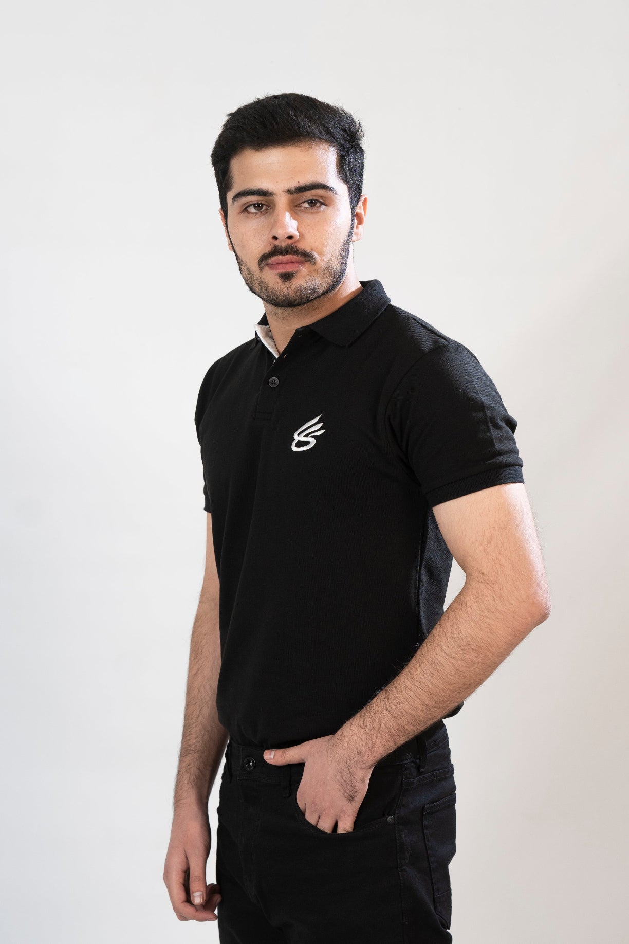 Man wearing a black polo shirt with a logo on a white background