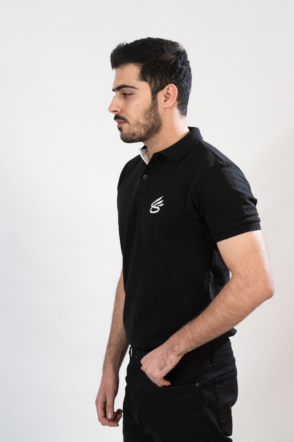 Man wearing a black polo shirt with a logo on a white background