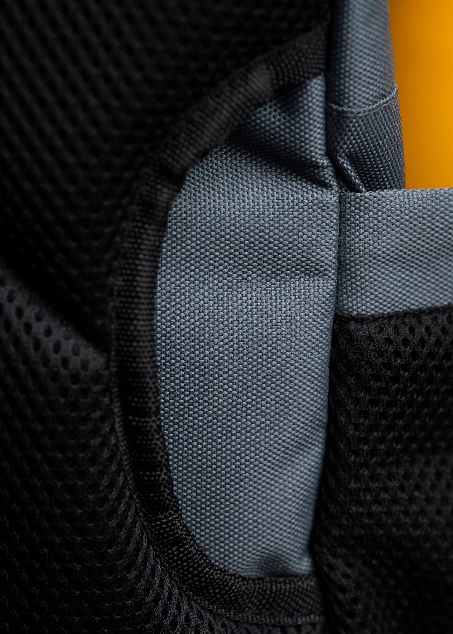 Close-up of the gray tactical backpack showing the woven fabric texture, breathable mesh side panel and bottle pocket
